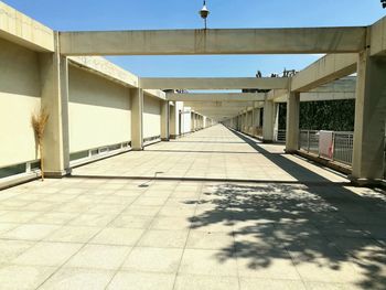 Empty footpath amidst buildings against sky on sunny day