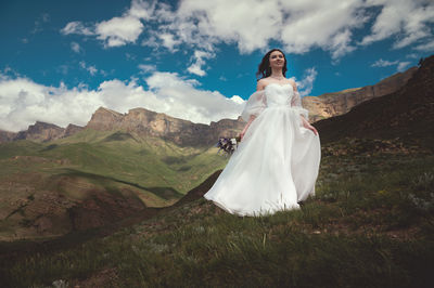 Bride in a white wedding dress walks in the green mountains on the grass, in the background there