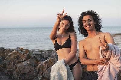 Portrait of young couple gesturing peace sign against sea