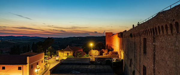 Illuminated buildings in town against sky at sunset