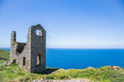 Old castle by sea against blue sky during sunny day