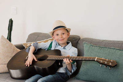 Boy smiling whilst playing guitar with a hat on at home