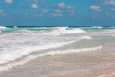 Waves rushing towards shore against sky