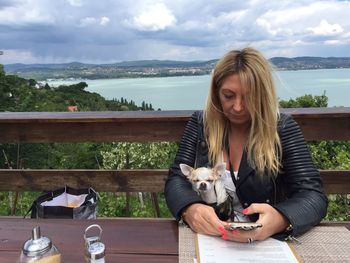 Woman with chihuahua using mobile phone against lake