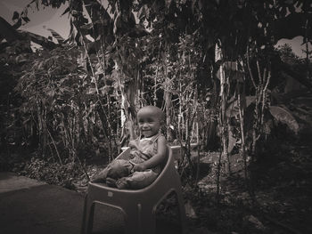Portrait of boy sitting by plants against trees