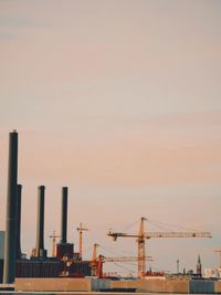 Cranes at construction site against sky during sunset