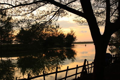 Silhouette trees by lake against sky during sunset