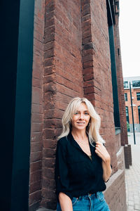 Portrait of smiling young woman standing against brick wall