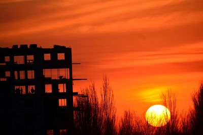 Silhouette built structure by sea against orange sky