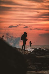 Silhouette men standing on beach against sky during sunset