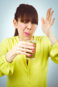 Woman having drink while standing against wall