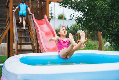 Full length of smiling girl playing on slide in swimming pool