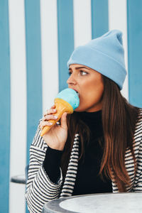 Young woman eating ice cream cone against at table