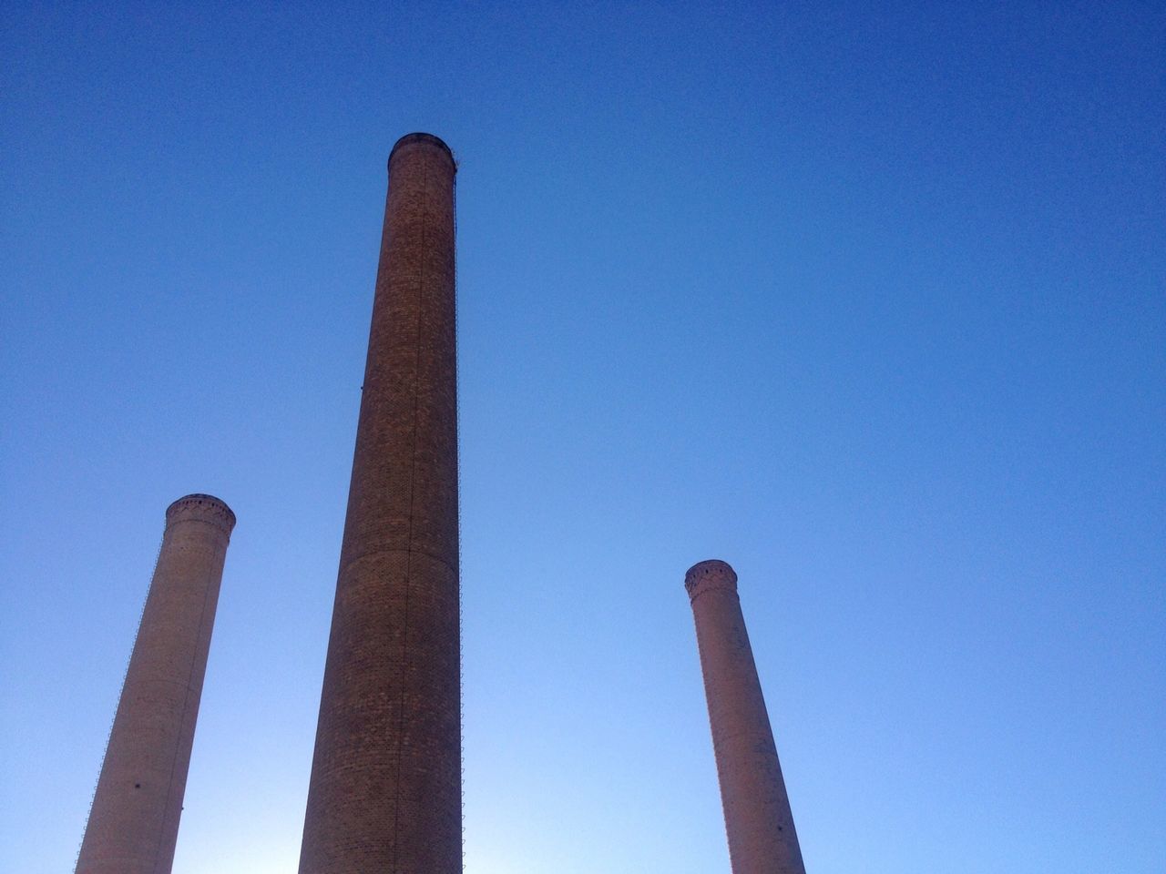 low angle view, clear sky, blue, smoke stack, built structure, industry, copy space, tall - high, factory, pole, architecture, no people, day, outdoors, tower, metal, sky, tall, architectural column, wooden post