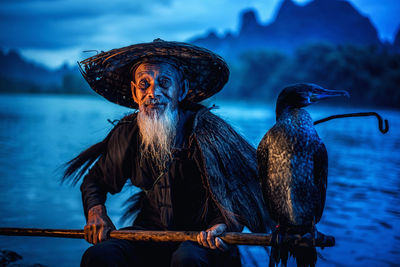 Bird perching on stick held by man in lake
