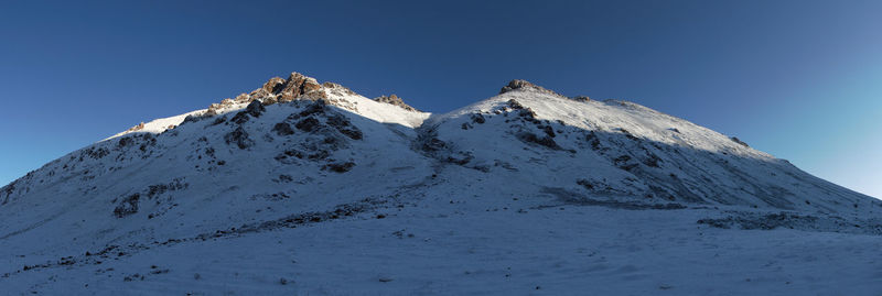 Low angle view of snowcapped mountains against clear blue sky