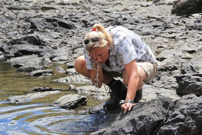 Full length of woman washing face with water at lakeshore