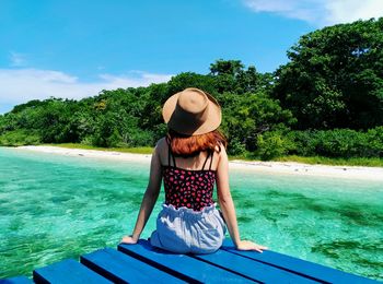 Young woman sitting on jetty over sea against sky