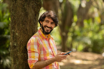 Young man with smartphone at day time with a green park in the background. mobile phone, technology,