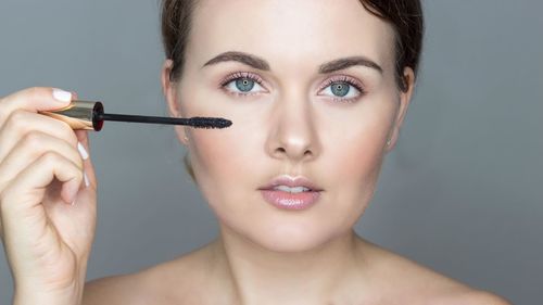 Close-up of young woman applying make-up against blue background