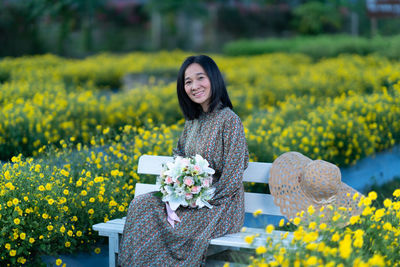 Portrait of a smiling young woman standing on yellow flowering plants