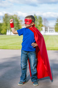 Full length of boy in superman costume standing on road against sky