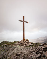 Cross on rock against sky