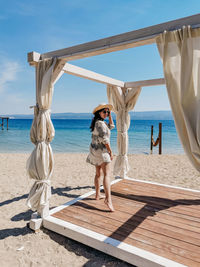 Young woman standing on wooden gazebo pavilion on beach on sunny day in summer.