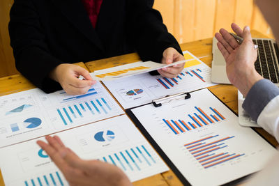 Cropped image of business colleagues analyzing graph on desk in office