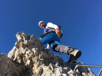 Low angle view of man rock climbing against clear blue sky