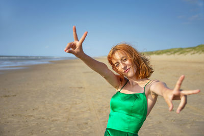 Young woman with arms raised standing at beach against sky