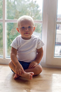 Child boy in a white t-shirt and shorts and blue eyes sitting on the windowsill