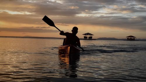 Rear view of silhouette man sailing in boat against sky during sunset