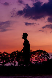 Rear view of man standing on rock against sky during sunset