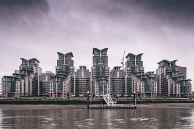 Buildings by river against sky in city during dusk