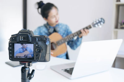 Close-up of camera with woman playing guitar in background