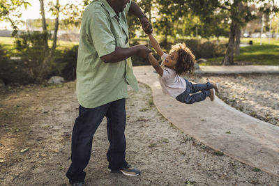 Midsection of playful father swinging son while playing at park