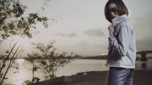 Side view of young woman standing against sky during sunset