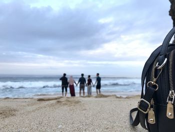 Close-up of bag with people standing on beach against sky