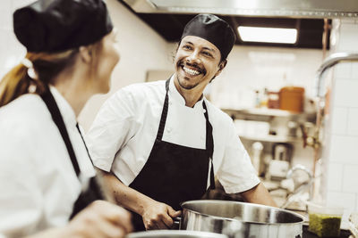 Glad manlig kock tittar på kvinnlig kock i restaurangkök