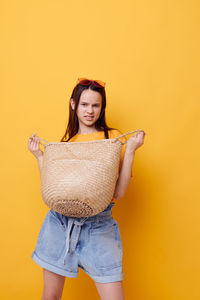 Portrait of young woman standing against yellow background