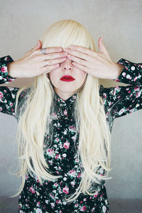 Woman covering eyes while standing against wall