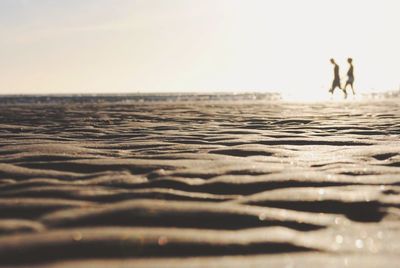 View of rippled sand with young couple holding hands in background