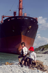 Two fashionable baby boys sit next to a large rio ship that ran aground off novorossiysk