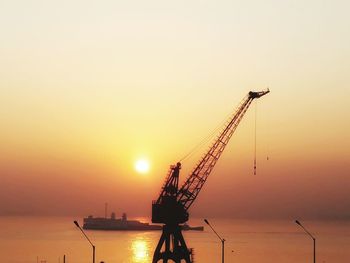 Silhouette cranes in sea against sky during sunset