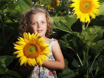 Portrait of smiling girl with sunflower standing against plants