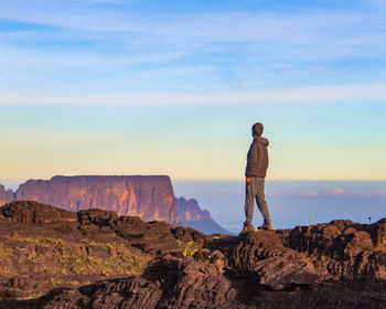 Rear view of man standing on rock against sky during sunset