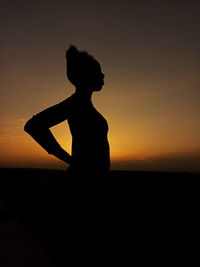 Silhouette woman standing on shore against sky during sunset