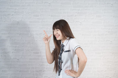 Happy young woman gesturing against wall