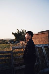 Side view of young man looking away against clear sky